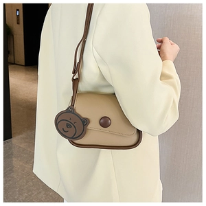 Detail of beige mini flap shoulder bag with brown trim and cute bear charm pendant