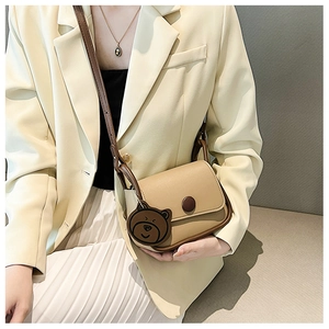 Detail of a beige saddle bag with brown trim and cute bear pendant on a suit