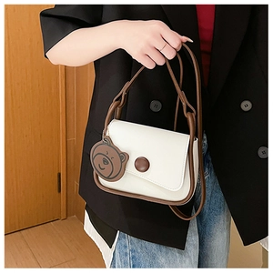 Detail of cream and brown saddle bag with bear charm carried by model in casual suit