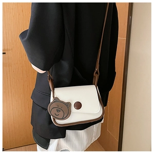 Detail of a retro saddle bag in white and brown leather with a cute bear charm