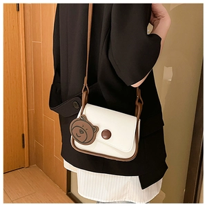 Minimalist cream shoulder bag with brown strap shown from a side view on a model