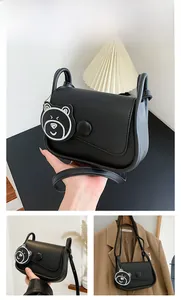 Detail of a black PU saddle bag showing the round buckle and cute bear pendant accessory
