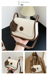 Detail view of cream saddle bag with brown trim and cute bear charm accessory