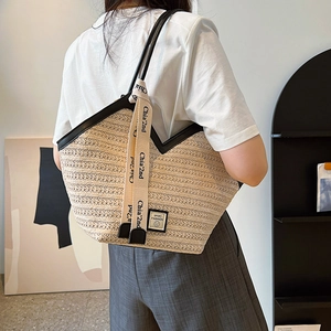 Large straw tote bag with black leather straps and decorative ribbon on female model