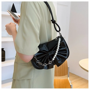 Sac à bandoulière noir avec nœud et chaîne en perles porté sur un costume vert clair