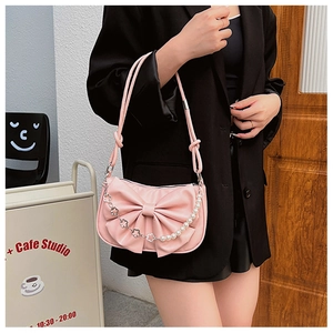 Pink shoulder bag detail with large bow and decorative pearl chain on black blazer