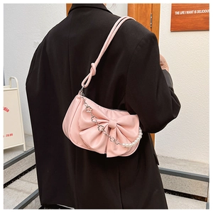 Détail du sac à bandoulière rose avec grand nœud et chaîne en perles sur costume noir