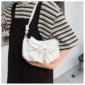Détail d'un sac à main blanc avec nœud, perles et chaînette en fleurs argentées