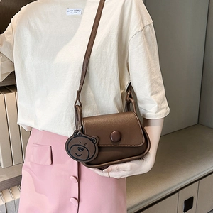 Brown leather crossbody bag with round buckle and bear charm on a female model