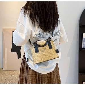 Détail du sac bandoulière en paille avec anses noires porté à l'épaule par un mannequin