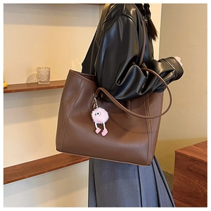 Brown matte leather tote bag with pink eye charm detail shown on a model in a warm room