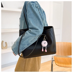 Detail of black leather tote bag featuring a pink plush charm and fine stitching