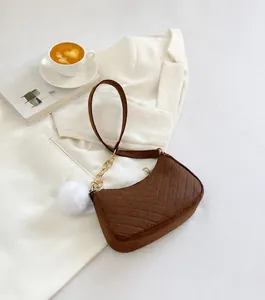 Close-up of brown chevron-quilted shoulder bag with gold chain and white pompom charm