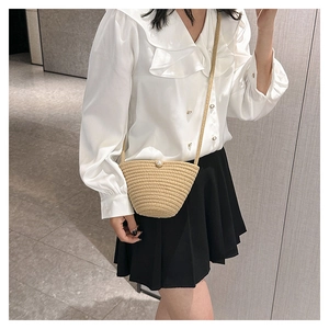 Dettaglio borsa a tracolla in paglia beige con bottone di perla indossata da modella