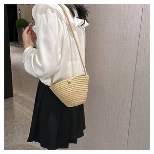 Dettaglio di borsa a secchiello in paglia beige intrecciata con bottone di perla e tracolla