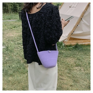 Dettaglio della mini borsa a secchiello viola intrecciata con bottone di perla e tracolla