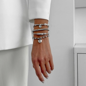 Detailed view of layered silver metal bracelets with heart pendant and faux pearl on wrist