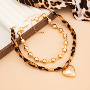 Close-up of golden heart pendant on leopard print necklace and metallic bead chain jewelry
