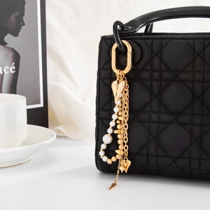 Detail eines goldenen Herz- und Perlenanhängers an einer schwarzen Stepptasche