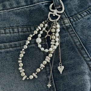 Detail einer mehrlagigen Kette mit silbernen Herzanhängern und Kunstperlen auf Jeanshose