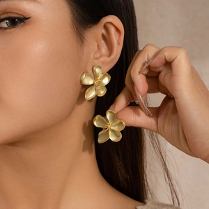 Close-up of matte gold five-petal flower earrings worn by a model for an elegant look