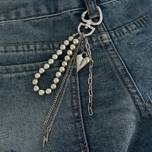 Silberne Punk-Hosenkette mit Herzanhänger, Perlen und Blitzdetail auf blauer Jeanshose