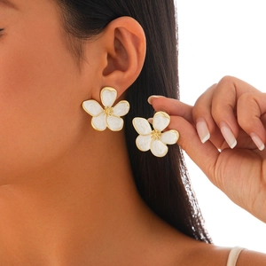 Macro view of white five-petal flower earrings with gold detailing on a model's ear