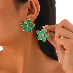 Detail of floral earring featuring green enamel petals and gold finish on model's ear