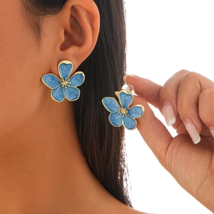 Close-up of blue enamel flower stud earrings with golden metal edges and petal details