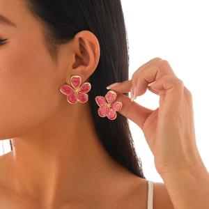Detailed view of pink floral earrings with gold trim worn by a model on white background