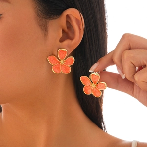 Macro shot of orange enamel flower earrings with gold leaf details on a model