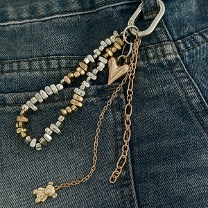 Detail einer mehrlagigen Hosenkette mit Herz- und Bärenanhängern auf Denim-Stoff