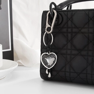Herz-Anhaenger aus grauem Acrylglas mit silbernen Tropfen an schwarzer Handtasche