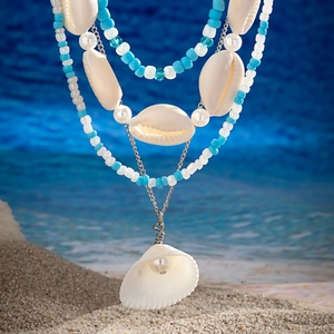 Close-up of ocean-style multi-layer necklace with shells and pearls on beach sand