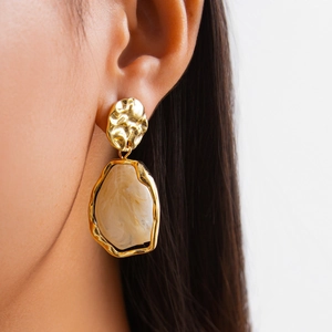 Gros plan de boucles d'oreilles dorées martelées avec pendentif résine marbre sur modèle