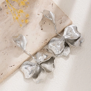 Macro detail of silver petal earrings with brushed metal texture on beige stone