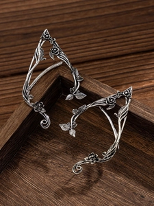 Detail of vintage silver elf ear cuffs featuring floral vine patterns on a dark wood box