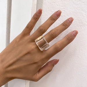 Gros plan d'une bague carrée en résine transparente sur une main, style minimaliste