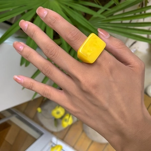 Détail d'une bague géométrique en résine jaune vif portée au doigt en plein air ensoleillé