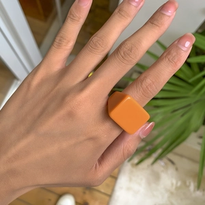 Détail d'une bague carrée en résine orange vif portée à la main dans un cadre lifestyle