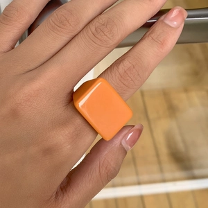 Détail d'une bague carrée en résine orange brillant portée pour un look géométrique audacieux