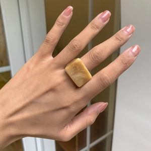 Gros plan d'une bague carrée en résine ambre avec texture marbrée au doigt
