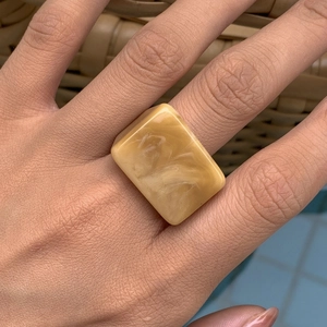 Détail d'une bague carrée en résine marbrée beige jaune portée au doigt pour femme