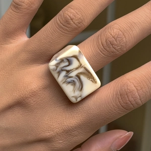 Détail d'une bague rectangulaire en résine avec texture marbrée crème et café au doigt