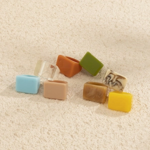 Vue de dessus de bagues géométriques en résine colorée sur un fond de sable texturé