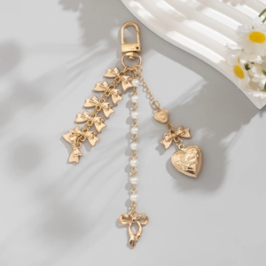 Porte-clés doré avec perles, médaillon cœur et nœuds sur un fond gris élégant