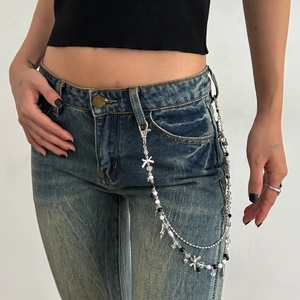 Detail van een gelaagde punk tailleketting met zilveren vlinders op een spijkerbroek