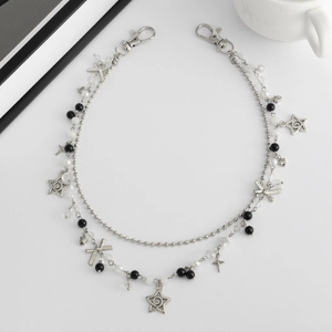 Detail van zilveren dubbele ketting met strik, sterbedels en kralen op witte achtergrond