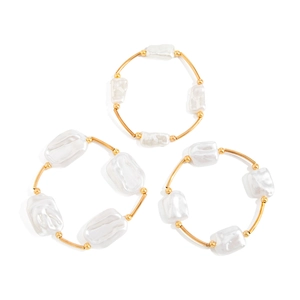 Set of three baroque pearl bracelets with gold curved metal tubes on a white background