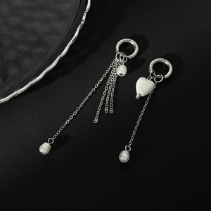 Détail de boucles d'oreilles asymétriques en perles baroques avec chaîne et cœur